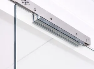 Electromagnetic door lock mounted on a frameless glass door, featuring a sleek brushed metal housing and secure magnetic plate, shown in a clean, bright installation with modern access control hardware.