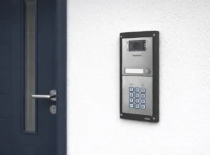 Video intercom mounted on a white exterior wall beside a modern front door, featuring a camera and keypad, ideal intercoms for home security and access control.